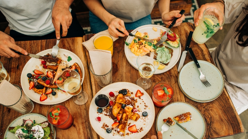 A group of four eat various brunch dishes with drinks including bubbly